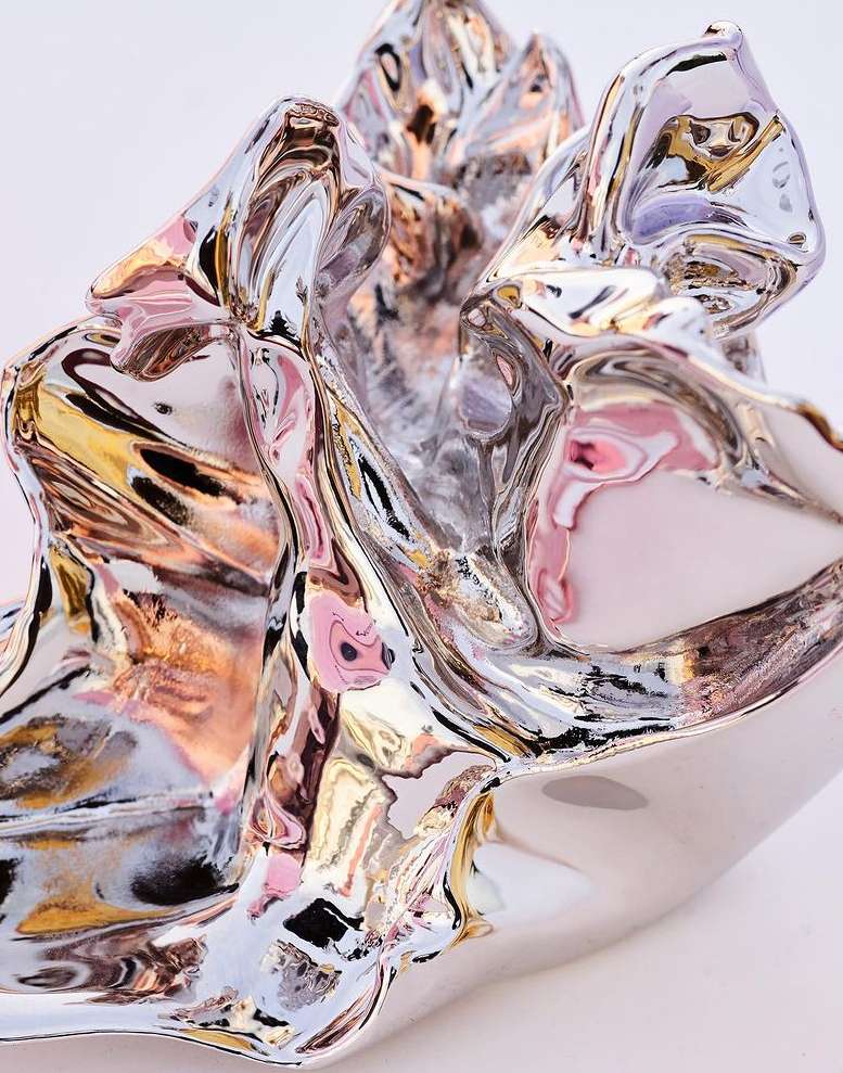 Abstract wavy artwork with silver and gold metallic reflections, creating a dynamic and fluid visual effect on a light background.