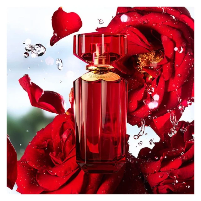 Red perfume bottle with a faceted lid set amongst red rose petals and water droplets creating an elegant and fresh beauty still life.
