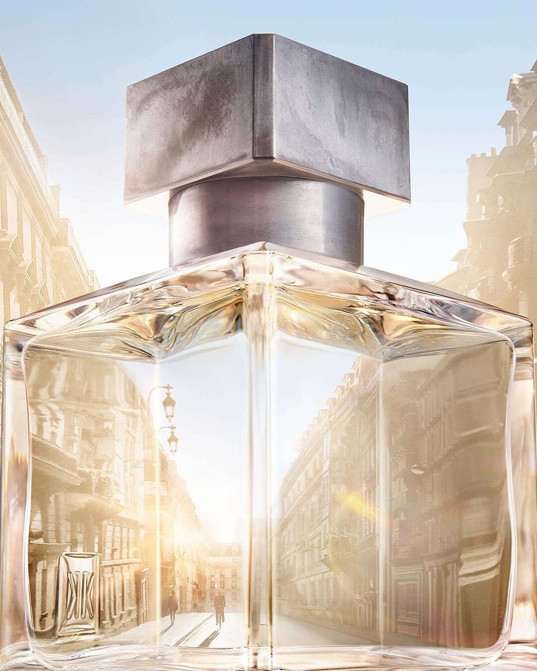 Close-up of a perfume bottle with a silver cap, reflecting an urban street scene of Paris, creating an illusion of depth and sophistication.