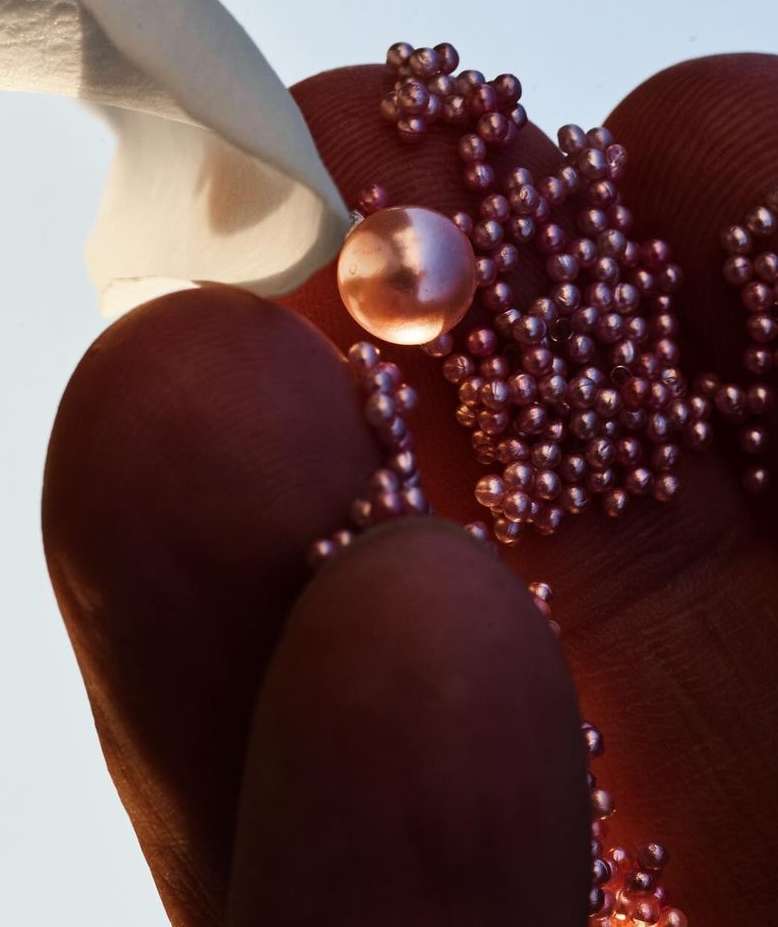 Close-up of a hand holding small, iridescent beads, with a blurred white object in the upper left, and a clean, light background.