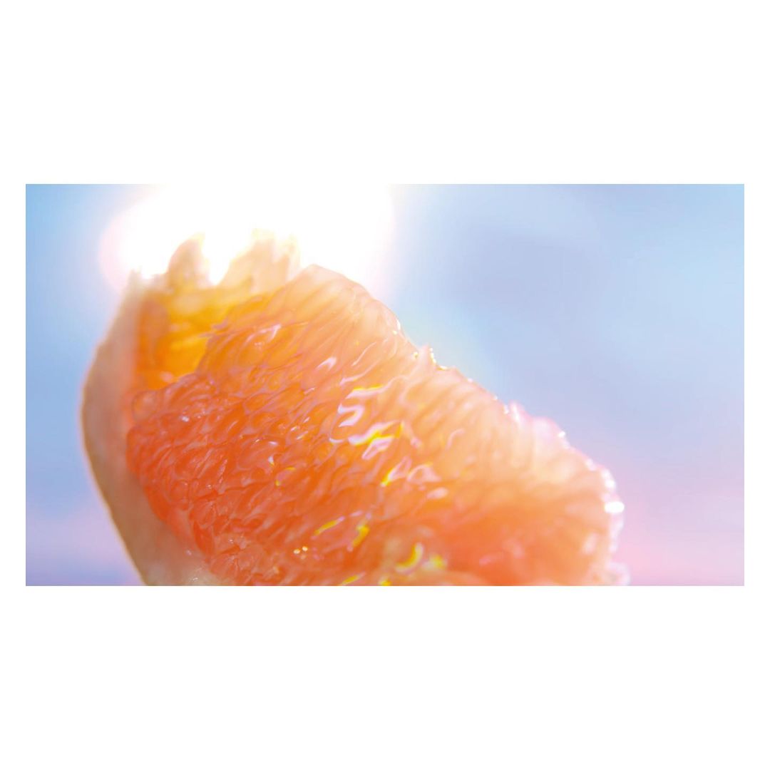 Close-up of an orange grapefruit segment showing the fruit's fleshy texture and bright color, set against a soft blue background with light.