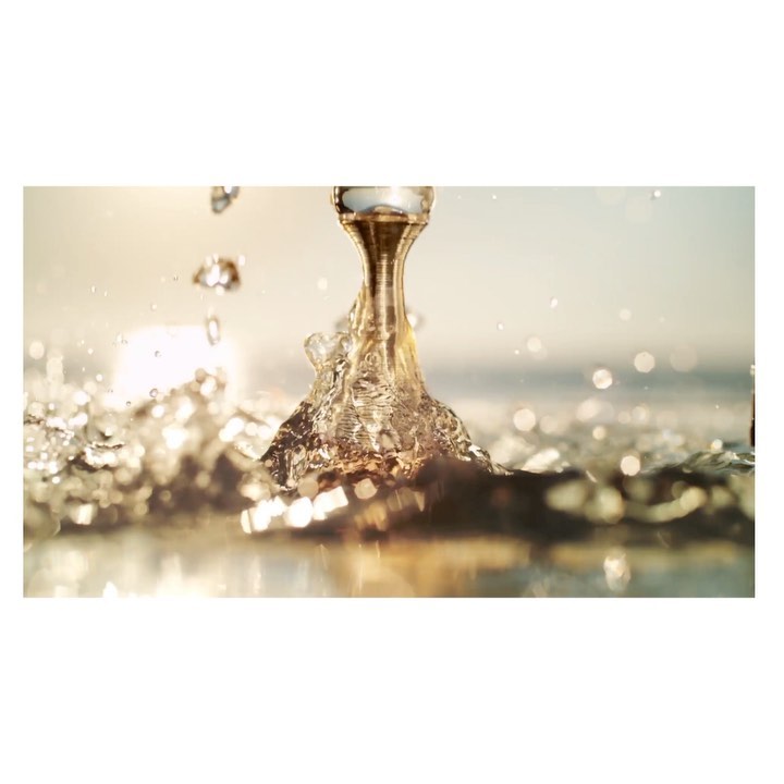Close-up of clear water pouring from a metallic spout, creating a splash against a soft, sunlit background with bokeh effects.