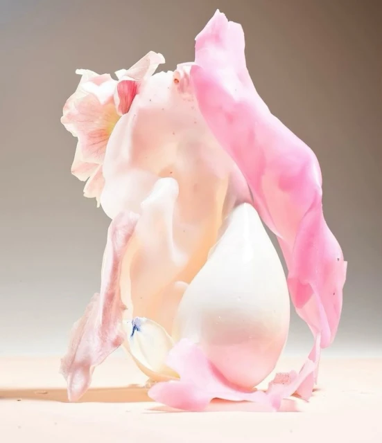 Still life of a white, egg-shaped object surrounded by pink and white floral petals, softly lit against a light brown background.