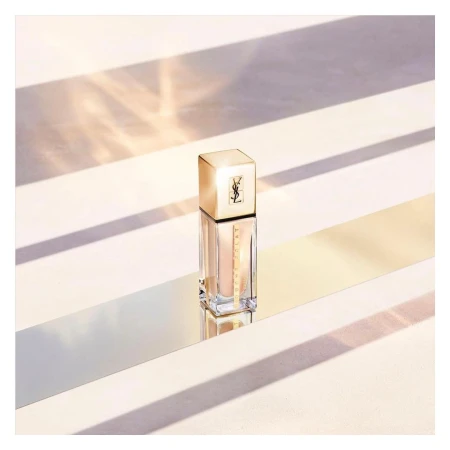 Elegant product shot of Yves Saint Laurent foundation with golden lid and clear bottle on a light surface with shadow stripes.
