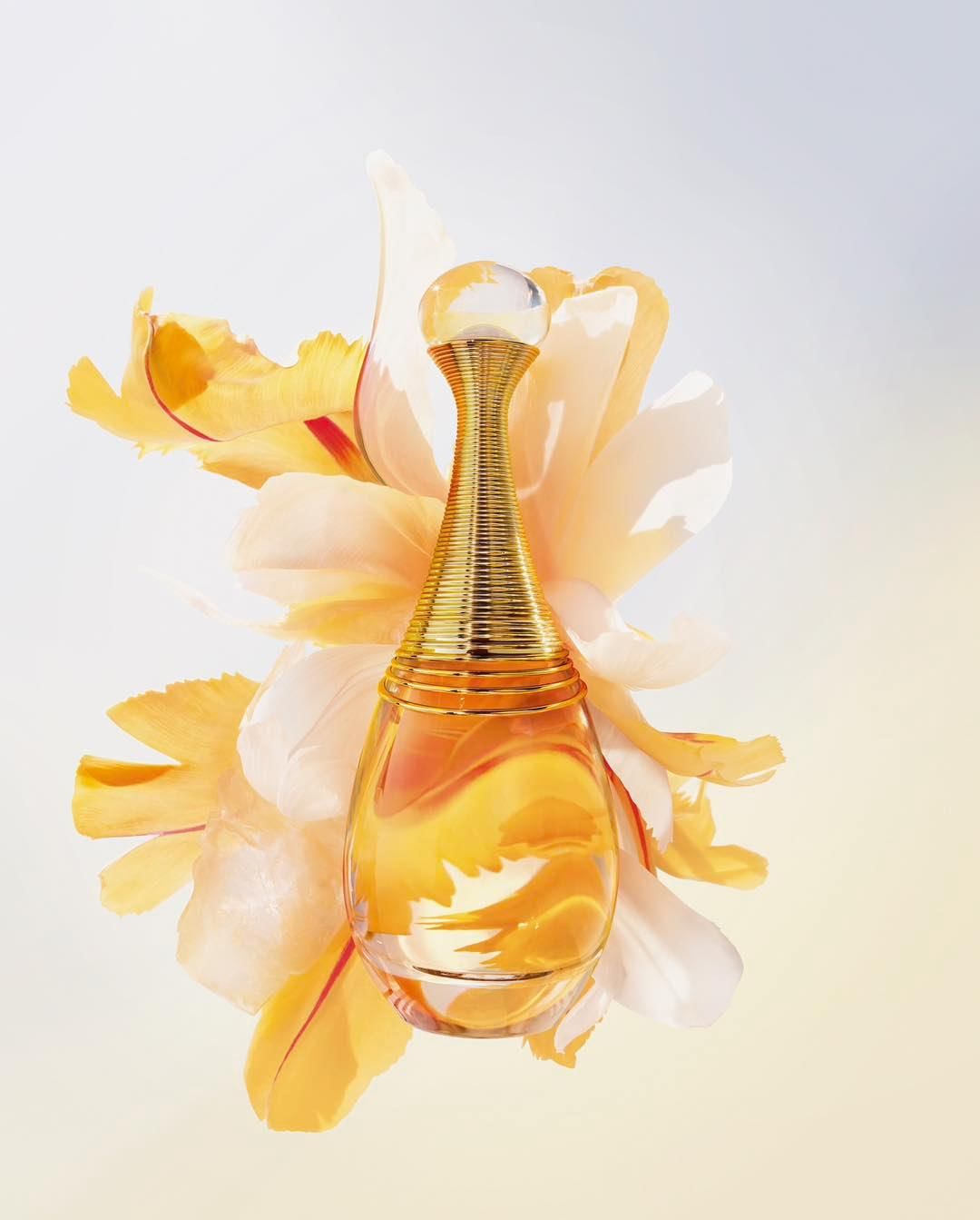 Elegant perfume bottle with gold accents surrounded by soft yellow flower petals on a light background in a beauty advertisement.