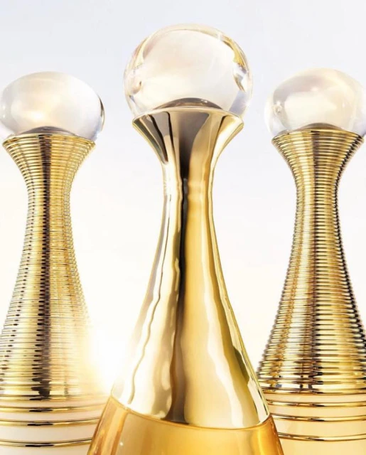 Three gold perfume bottles with glass ball tops stand on a white surface against a bright white background in a beauty product shot.