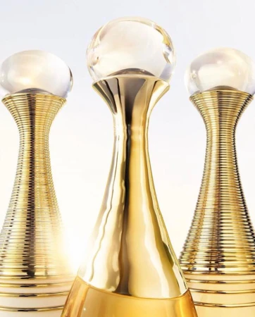 Three gold perfume bottles with glass ball tops stand on a white surface against a bright white background in a beauty product shot.