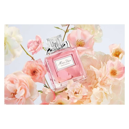 Close-up of a pink Miss Dior perfume bottle surrounded by pale pink and white roses on a light background, fashion, beauty, product photography.
