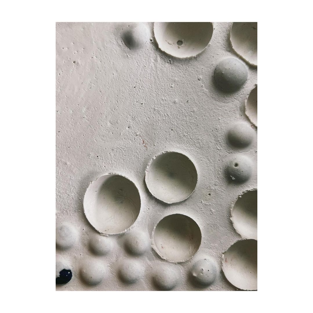 Abstract textured surface with spherical and hemispherical indentations in off-white tones, creating a tactile, minimalist composition.