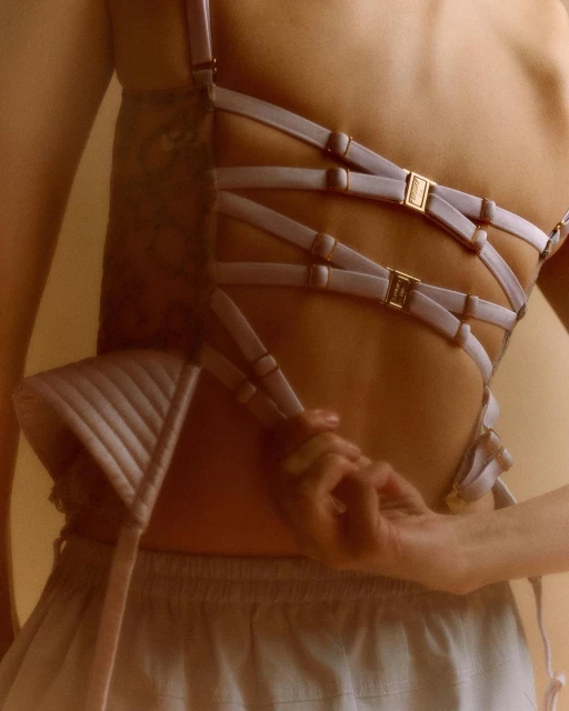 Close-up of a partially-dressed woman's back featuring lilac lingerie straps and skirt, revealing a tattoo and fair skin tone.