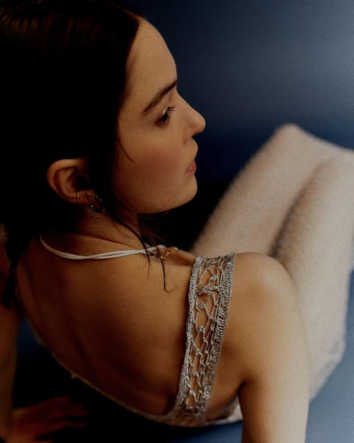 Profile portrait of a serene adult woman with dark hair in a light dress against a blue background, showcasing beauty and fashion.