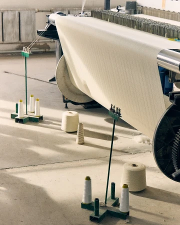 Textile manufacturing machine processes fabric and yarn in an industrial setting, showcasing production and fiber materials with neutral tones.