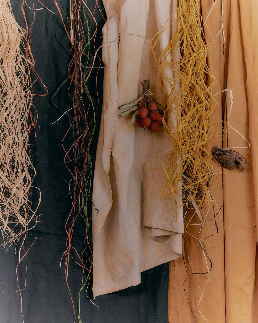Still life featuring draped fabric, straw, and dried leaves creating a textured, organic composition with neutral and earthy tones.