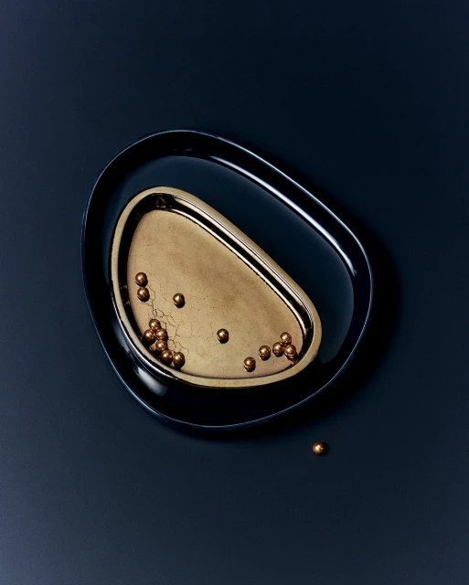 Elevated view of two oval serving trays. One dark-blue, one gold, some copper-colored metallic spheres scatter across the gold tray and surface.