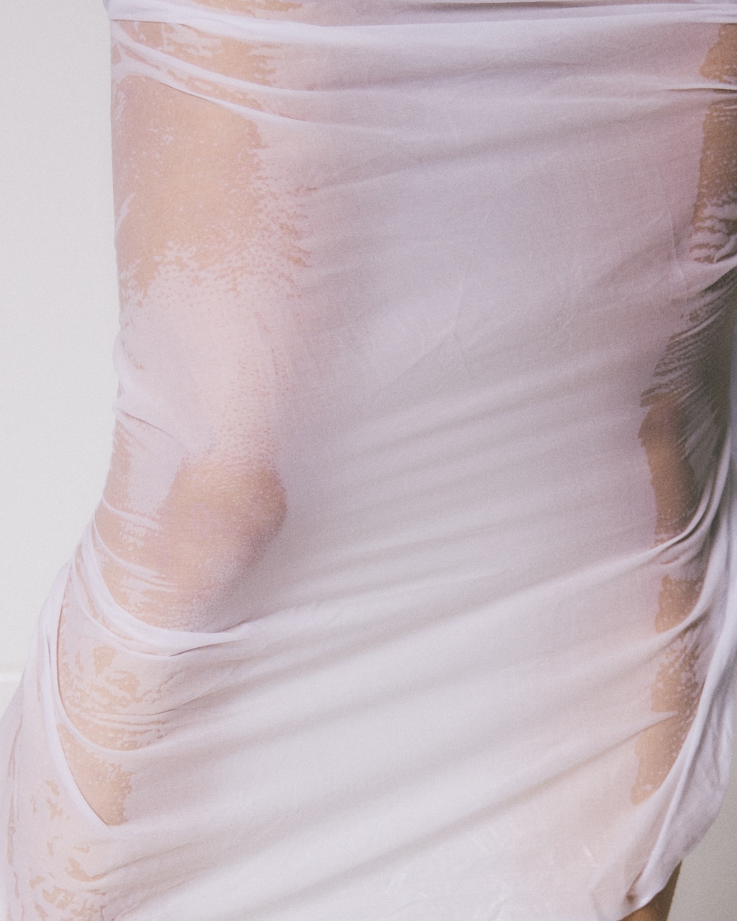 Torso of an adult woman wrapped in a transparent, wet, white fabric. The background is a solid white, with soft lighting.