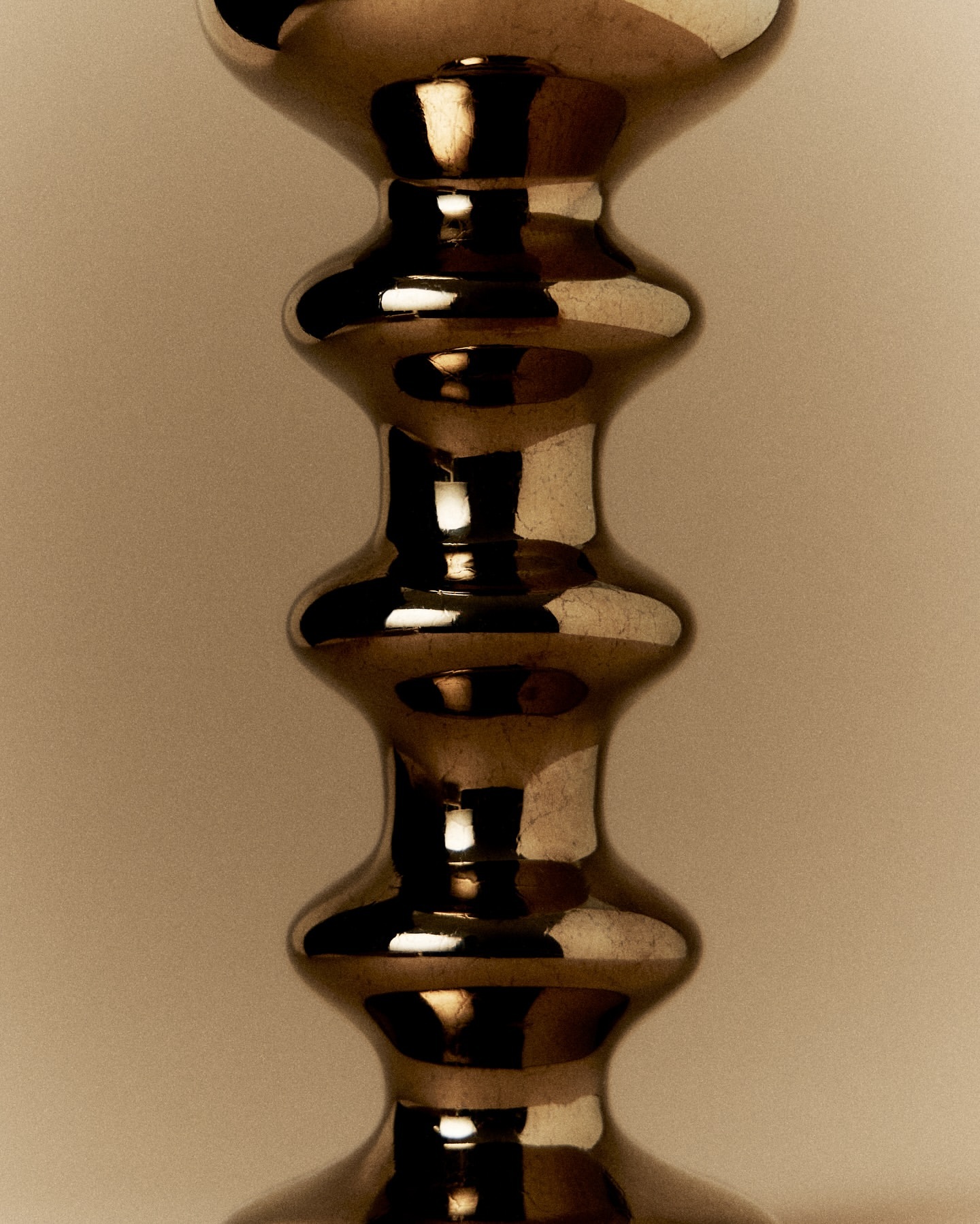 Close-up studio shot of a decorative metal candlestick with multiple curves and a reflective surface against a neutral backdrop.