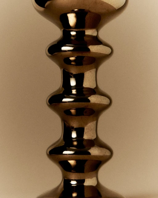 Close-up studio shot of a decorative metal candlestick with multiple curves and a reflective surface against a neutral backdrop.