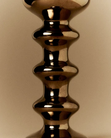 Close-up studio shot of a decorative metal candlestick with multiple curves and a reflective surface against a neutral backdrop.