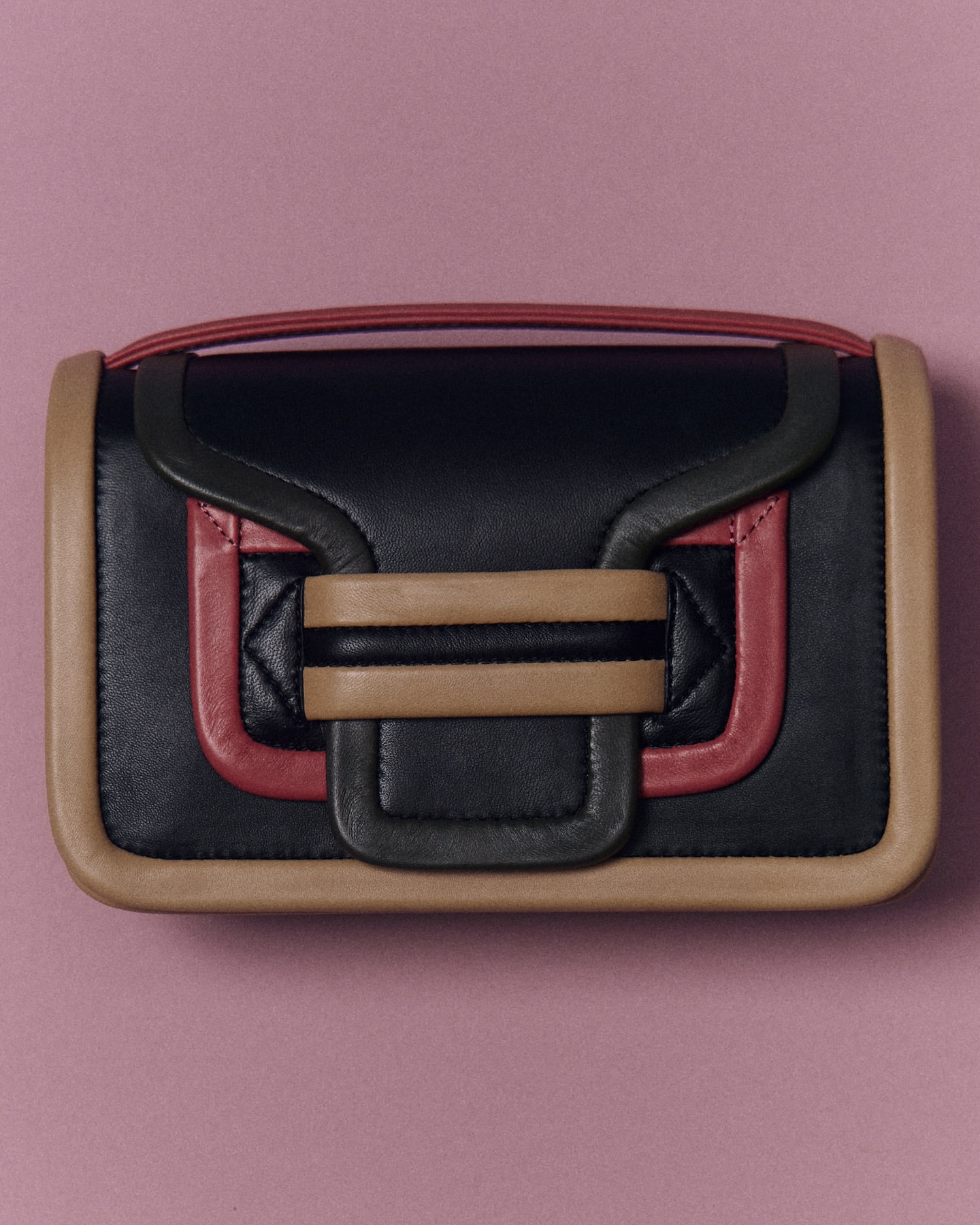 Studio shot of a stylish black leather handbag with tan and pink trim against a pink backdrop. Minimalist fashion accessory.