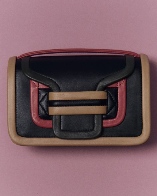 Studio shot of a stylish black leather handbag with tan and pink trim against a pink backdrop. Minimalist fashion accessory.
