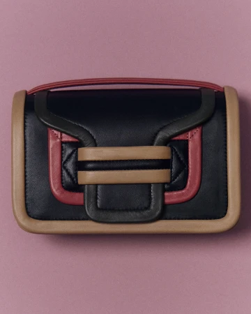 Studio shot of a stylish black leather handbag with tan and pink trim against a pink backdrop. Minimalist fashion accessory.