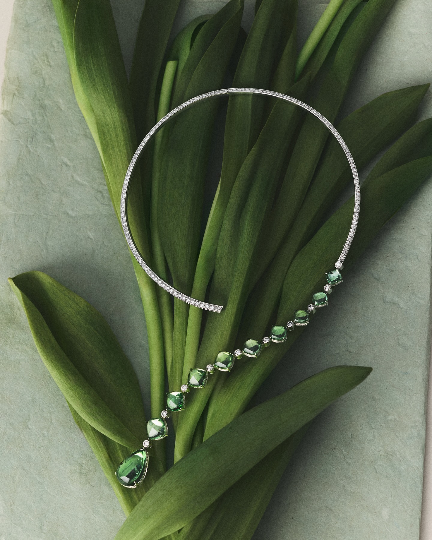 Elegant diamond and green gemstone necklace showcased on fresh green tulip leaves, jewelry fashion product shot, luxury gemstone necklace.
