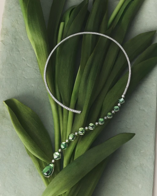 Elegant diamond and green gemstone necklace showcased on fresh green tulip leaves, jewelry fashion product shot, luxury gemstone necklace.