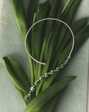 Elegant diamond and green gemstone necklace showcased on fresh green tulip leaves, jewelry fashion product shot, luxury gemstone necklace.