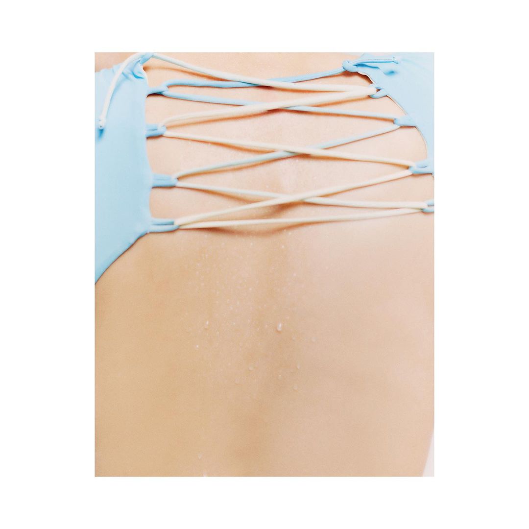 Close-up of a person's back with a blue swimsuit or top featuring criss-cross straps, set against a plain white backdrop.