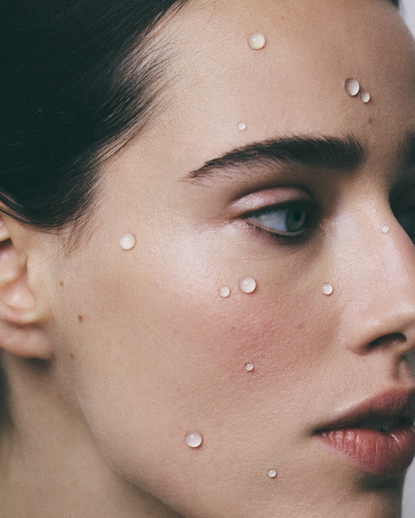 Close-up portrait of a woman's face with small water droplets on her skin, photographed by Florie Berger in Paris.