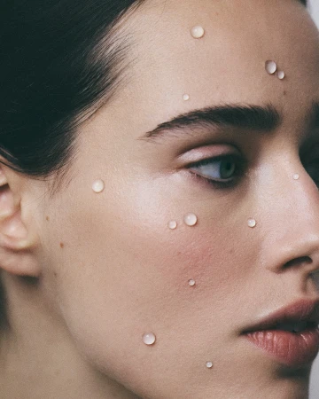 Close-up portrait of a woman's face with small water droplets on her skin, photographed by Florie Berger in Paris.