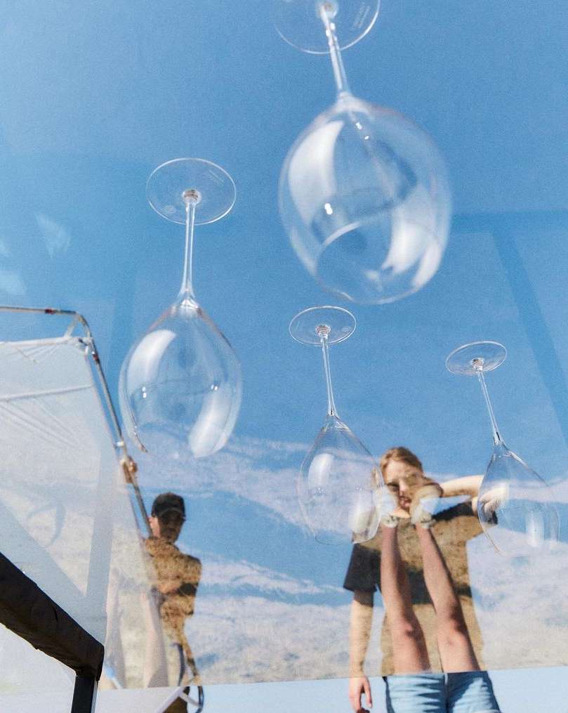 Low-angle shot of four wine glasses hanging upside down, an adult male and female, and a partial view of a patio.
