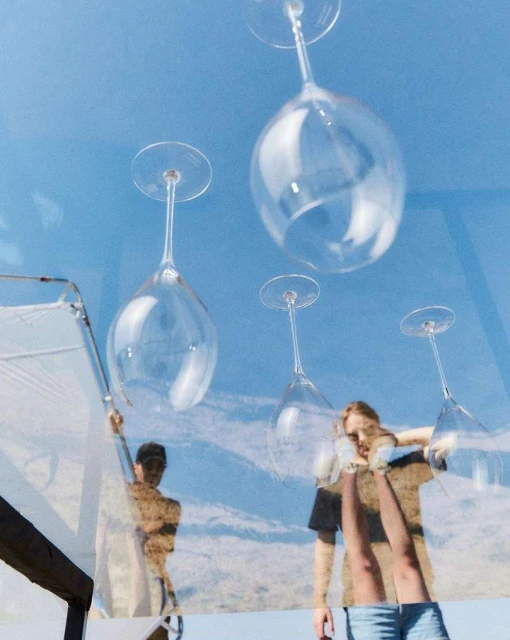 Low-angle shot of four wine glasses hanging upside down, an adult male and female, and a partial view of a patio.