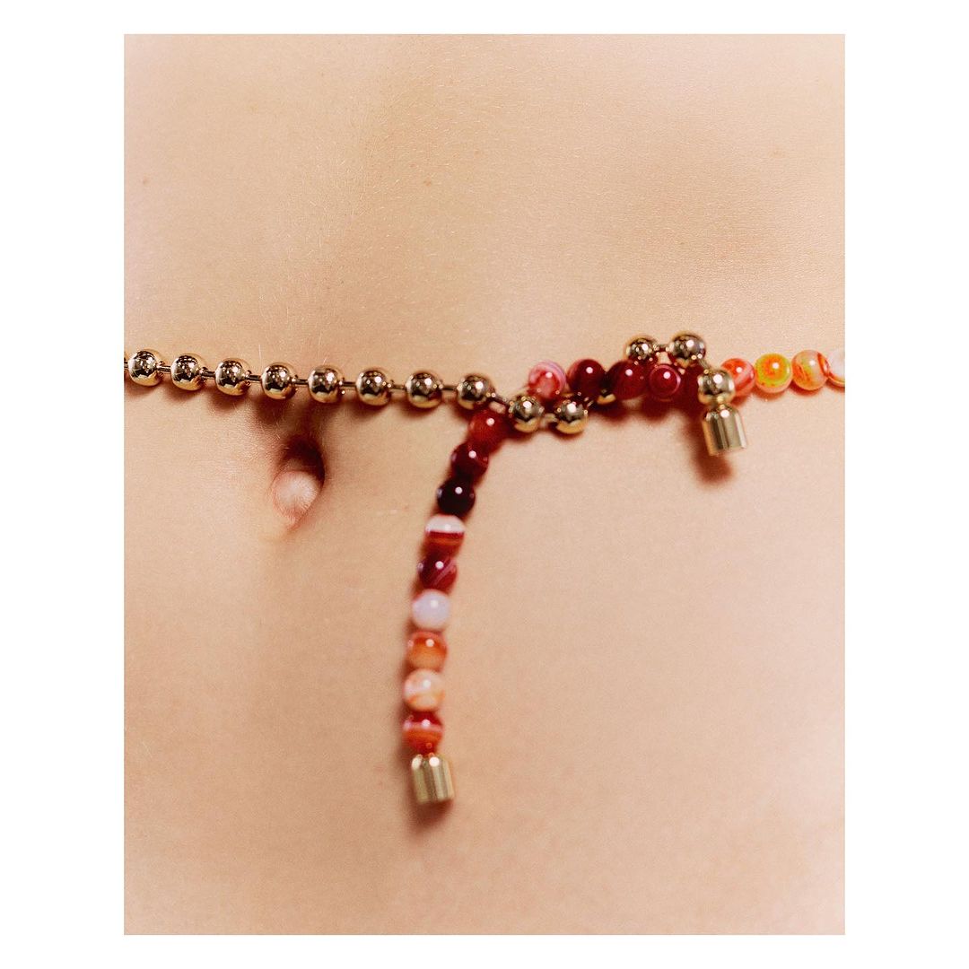 Waist-level shot of the torso of a person with an agate beaded waist chain, featuring a ball chain with gold-colored spheres.