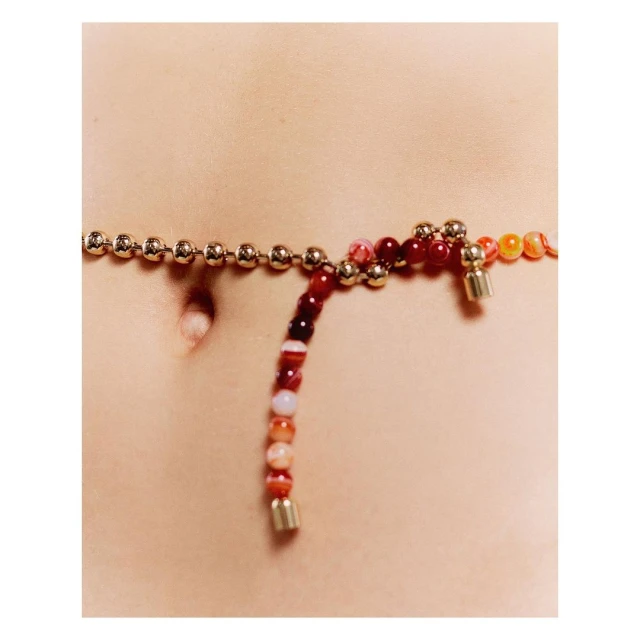 Waist-level shot of the torso of a person with an agate beaded waist chain, featuring a ball chain with gold-colored spheres.