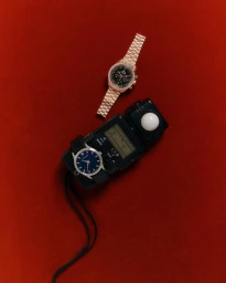 Two luxury wristwatches and a light meter on a rich red velvet textured background