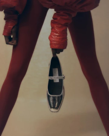 Close-up of a person in red leggings holding a Mary Jane shoe between legs against a neutral background