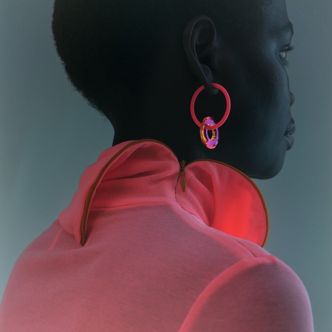 Profile shot of an African-descent woman wearing a pink dress and hoop earrings in a studio with muted lighting and a neutral background.