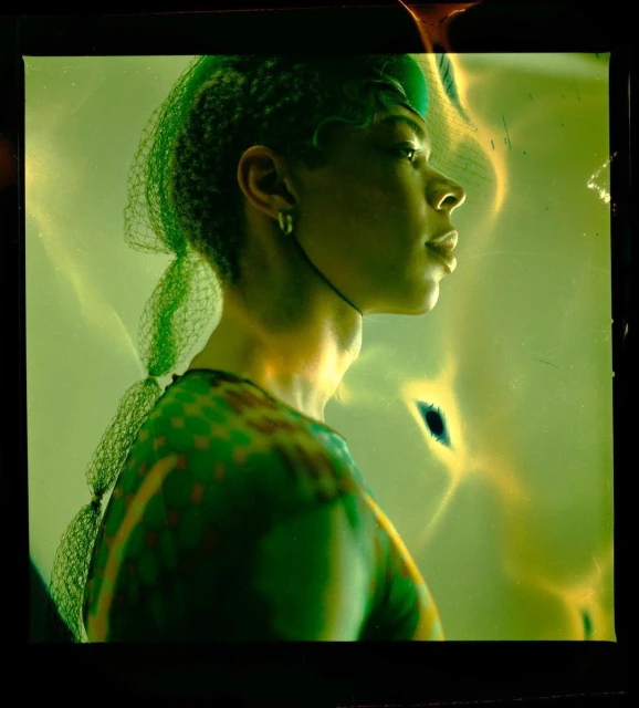 Portrait of a woman in profile wearing a patterned top and netting in a studio with green and yellow lighting, shot with shallow depth of field.