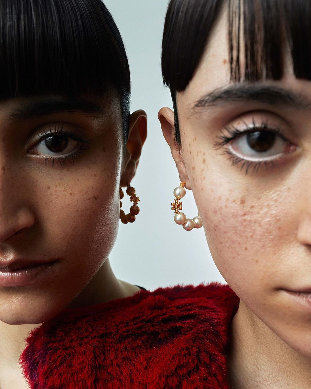 Close-up shot of two women with dark hair and pearl earrings, posing closely together. Red fur garment visible on the women's shoulders.