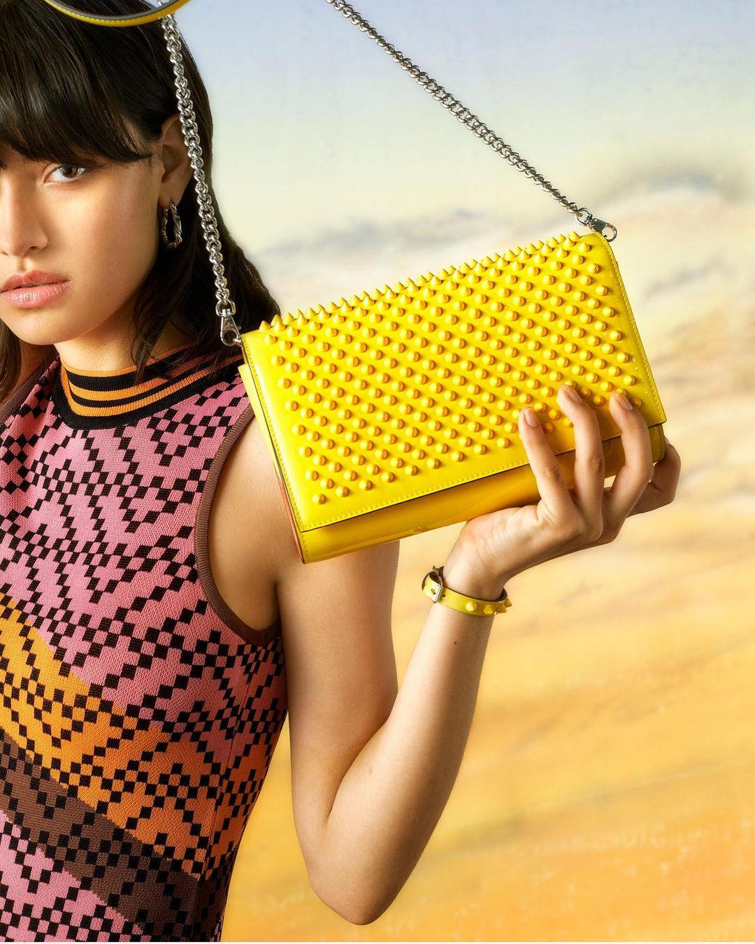 Studio shot of an Asian woman in patterned tank top holding a yellow studded purse with silver chain. Fashion and beauty.