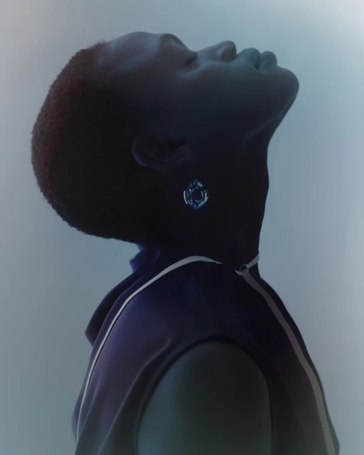 Portrait of a Black adult female wearing an earring looking up. She is wearing a dark blue sleeveless top with white stripes.