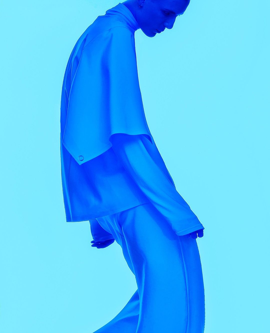 Monochromatic blue fashion shot: person in matching blue suit and button-down shirt posing in studio against a pale blue backdrop.