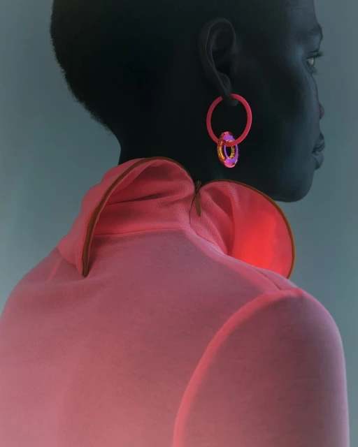 Back view of dark-skinned woman with hoop earrings wearing salmon-colored top. Her head is in profile to the right.