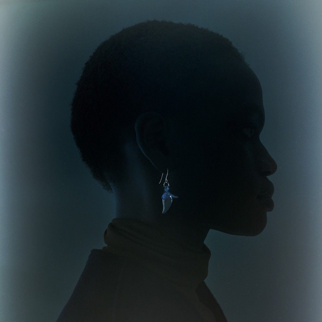 Silhouette of dark-skinned woman wearing jewelry earring, against a dark-blue-toned background in a studio-lit side-view portrait.