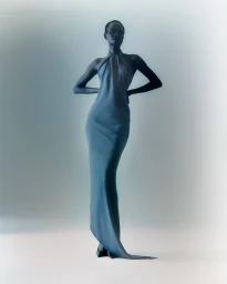 Black model in a long blue halter dress posing against a soft gradient grey studio background by photographer Fofo Altinell.