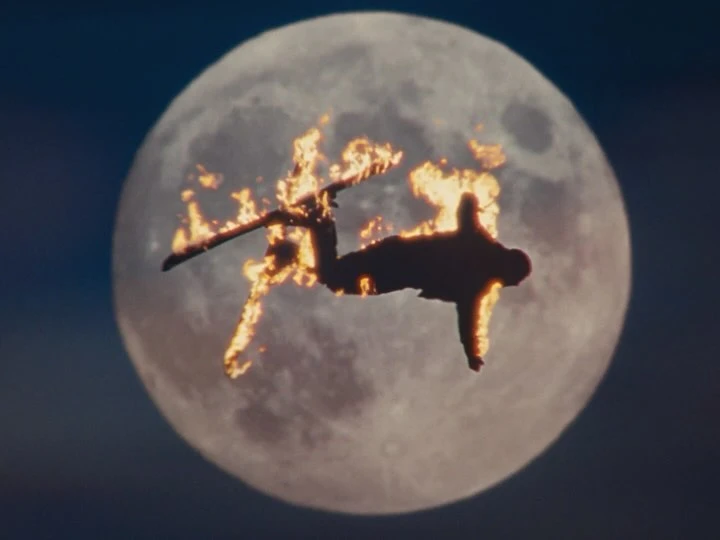 Silhouette of a person on skis engulfed in flames jumping against the backdrop of a full moon at night creating a dramatic visual.