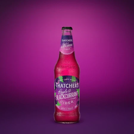 Bottle of Thatcher's Apple & Blackcurrant Cider with condensation on a purple background. The cider bottle is centered.