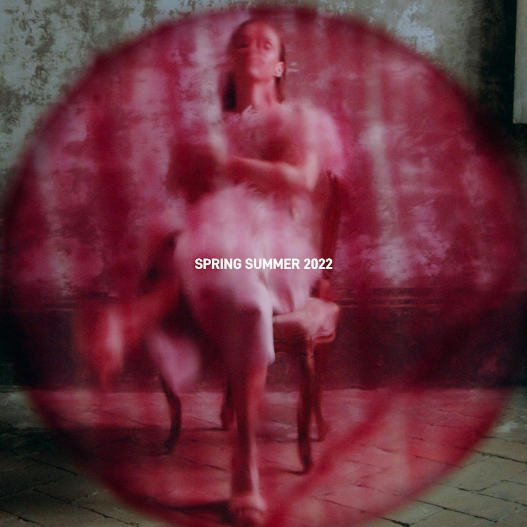 Fashion shot of a woman in a pink dress sitting in a vintage chair, captured with soft focus and muted colors, emphasizing textures.