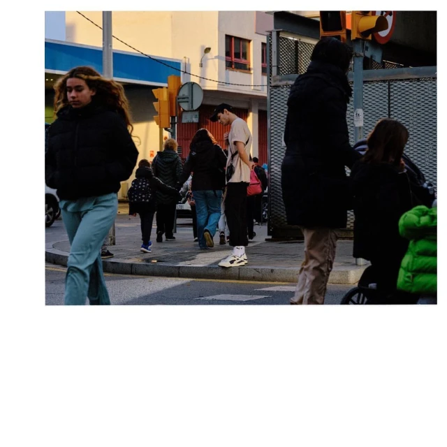 Street scene featuring a young woman in a black jacket and jeans walking towards the camera, with other pedestrians and buildings in the background.